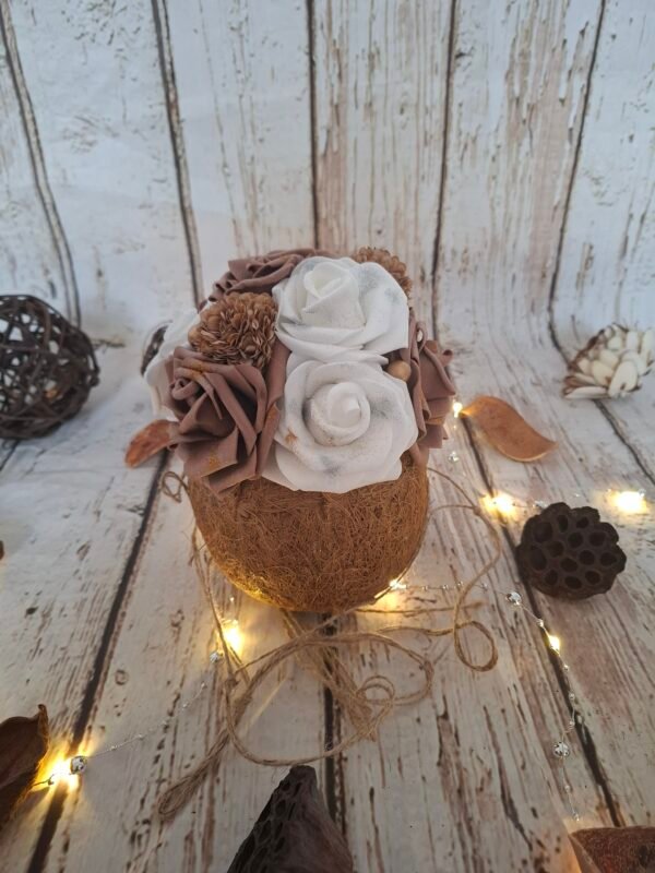 Coco mystique, composition florale dans une noix de coco avec des roses blanches, des roses chocolat, des minis hortensias marron, des perles dorées et des paillettes pour une ambiance magique et élégante.