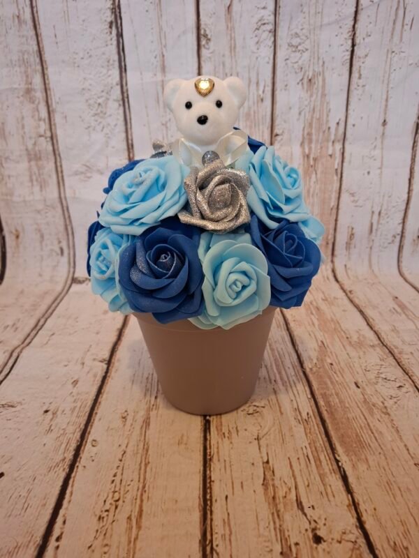 Composition florale Calin bleu avec un ourson blanc et des roses pailletées argentées dans des tons de bleu