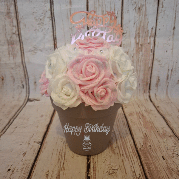 Composition florale Éclat d’anniversaire avec des roses roses claires et blanches, des roses avec strass, un décor Happy Birthday et personnalisation du pot.
