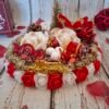 Féérie festive, centre de table avec mousse blanche, sapin doré, pomme de pin, roses blanches, cercles en bois, perles dorées pailletées, fleur rouge, guirlande, traineau, bonbon et canne à sucre pour Noël.