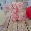 Composition florale Ourson d'amour avec des roses blanches et roses claires, et une décoration en forme de cœur.