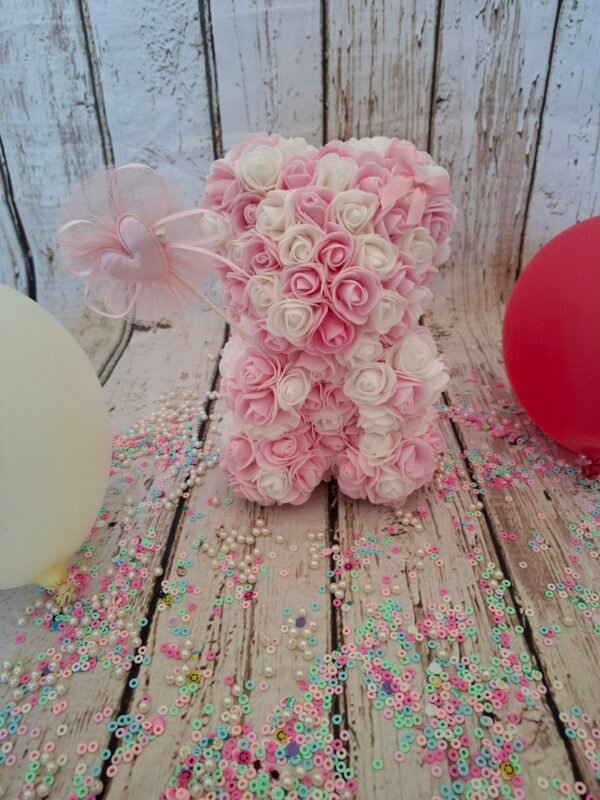 Composition florale Ourson d'amour avec des roses blanches et roses claires, et une décoration en forme de cœur.