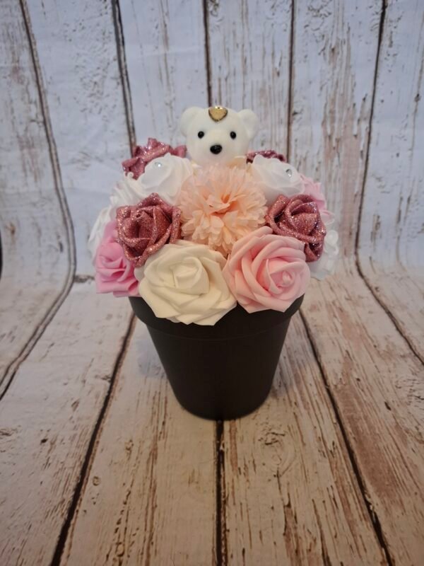 Composition florale Tendre Ourson avec un ourson blanc, des roses pailletées rose, des hortensias rosés, des roses blanches, des roses claires et des roses strass rose foncé.