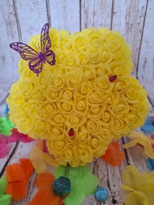 Fleur Timaiika jaune avec mini roses en mousse, décorée de coccinelles et papillon en papier, posée sur support en bois.