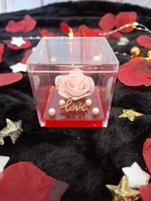 Rose blanche pailletée, fond en résine rouge et perles nacrées, symbole d’amour éternel.