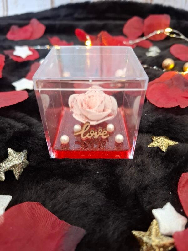Rose blanche pailletée, fond en résine rouge et perles nacrées, symbole d’amour éternel.