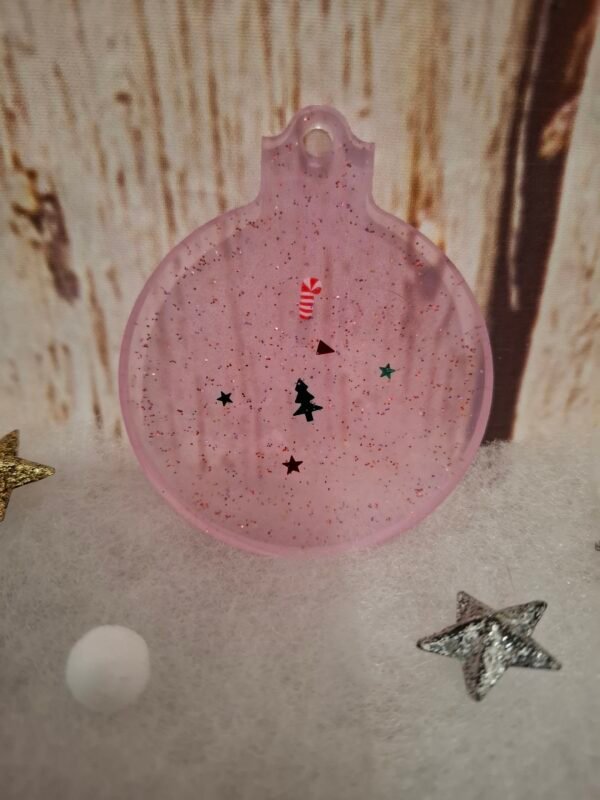 Décor de Noël artisanal : boule rose avec accessoires festifs et paillettes étincelantes.