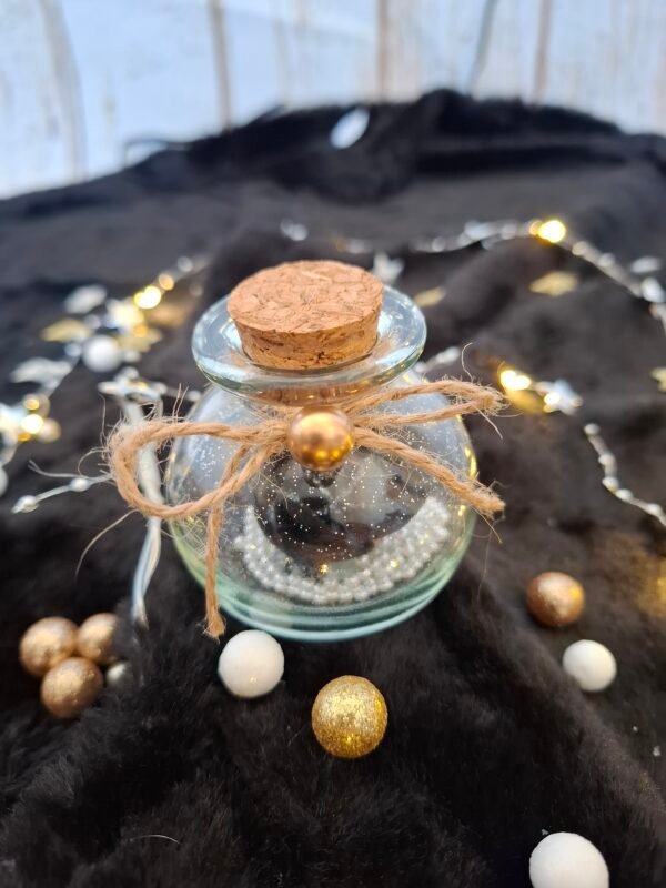 Flacon en verre avec rose noire, paillettes argentées et petites perles blanches.