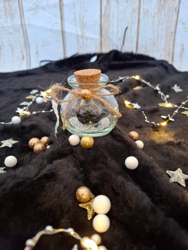 Flacon décoratif avec rose sombre, éclats scintillants et touches dorées élégantes.