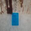 Accessoire unique en résine bleue, scintillant grâce à ses paillettes, rectangle de 2,9 cm de hauteur et 1,5 cm de largeur, idéal pour personnaliser trousseaux et sacs avec charme.