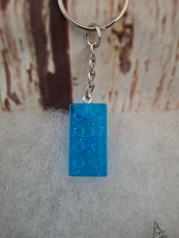 Accessoire unique en résine bleue, scintillant grâce à ses paillettes, rectangle de 2,9 cm de hauteur et 1,5 cm de largeur, idéal pour personnaliser trousseaux et sacs avec charme.