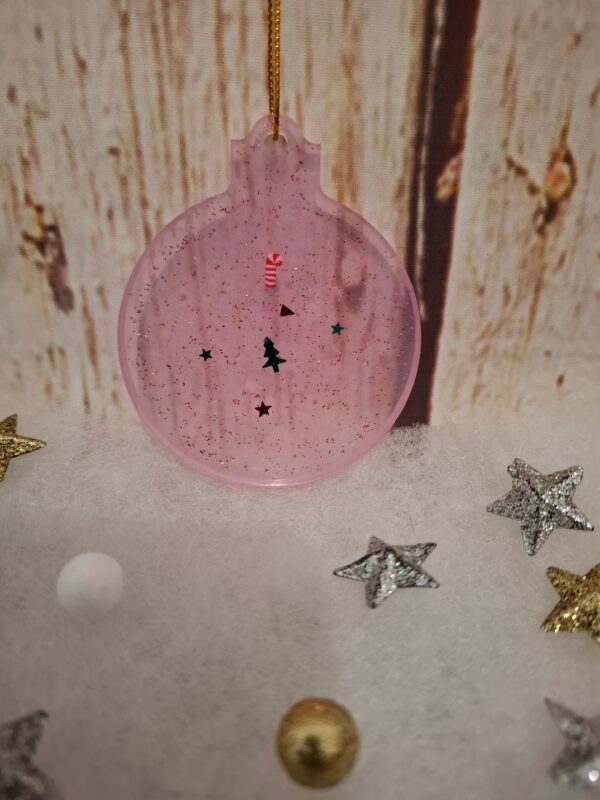 Création unique en résine : boule plate rose avec ornements de fête et éclats brillants.