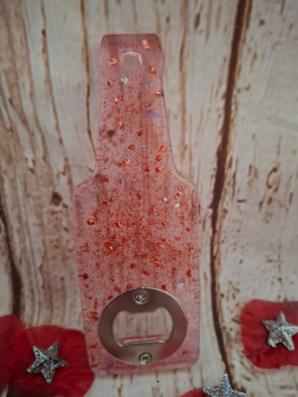 decapsuleur-personnalise-paillettes-pierres-artisanale-cadeau-apero-original-faitmain-surmesure-001 Décapsuleur artisanal rouge-rose en résine, forme de bouteille, avec paillettes et petites pierres, idéal pour vos apéritifs et moments conviviaux.