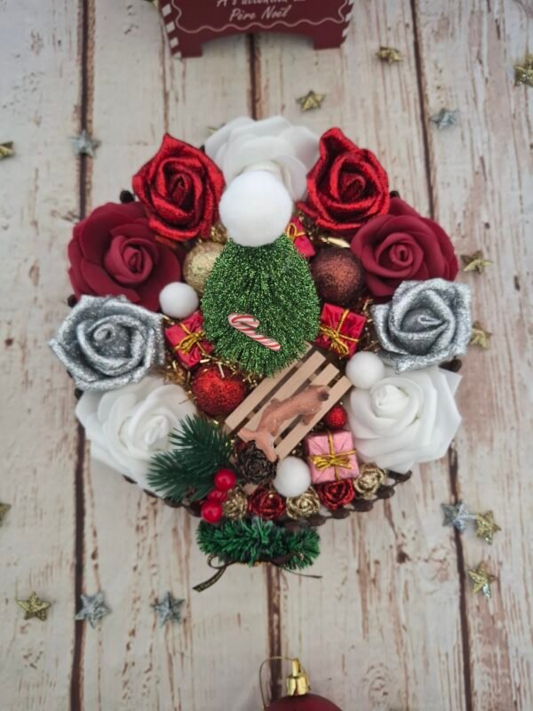 Création Douce Nuit de Noël mettant en scène un sapin décoré, roses argentées pailletées et rouges, boules de Noël rouges et bronze, petite luge avec une biche, barrière en bois et touches de neige artificielle pour une décoration chaleureuse.