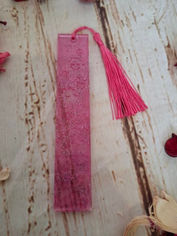 Petit marque-pages décoratif en résine rose, avec paillettes et pompon assorti, parfait pour personnaliser vos moments de lecture.