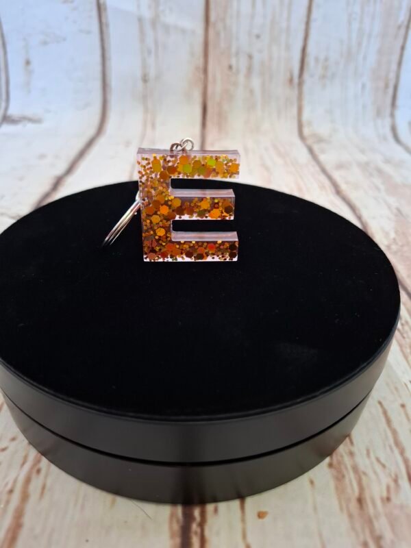 Initiale E façonnée à la main en résine, légère et élégante, avec un petit pompon assorti, parfaite pour offrir ou ajouter une touche originale à vos accessoires du quotidien.