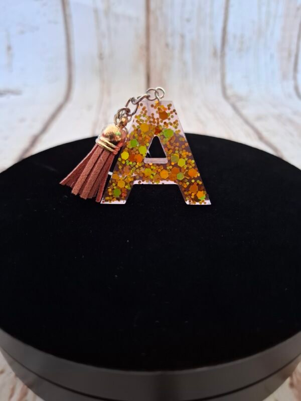 Création artisanale A en résine avec touches scintillantes, ornée d’un pompon, idéale pour un cadeau unique.