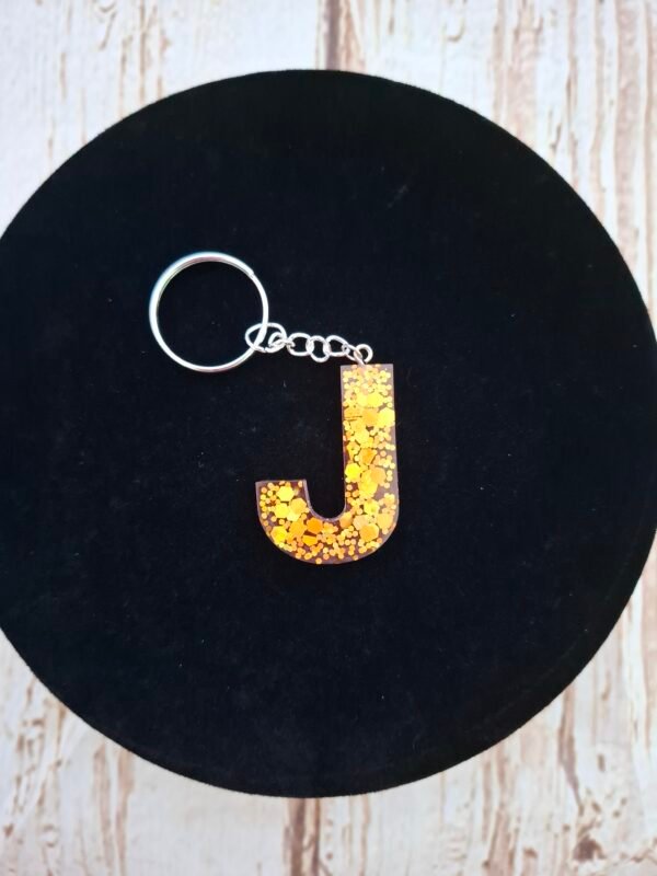 Porte-clés personnalisé lettre J de Jaelys, pièce unique aux nuances rose poudré avec inclusions dorées étincelantes et breloque textile assortie.