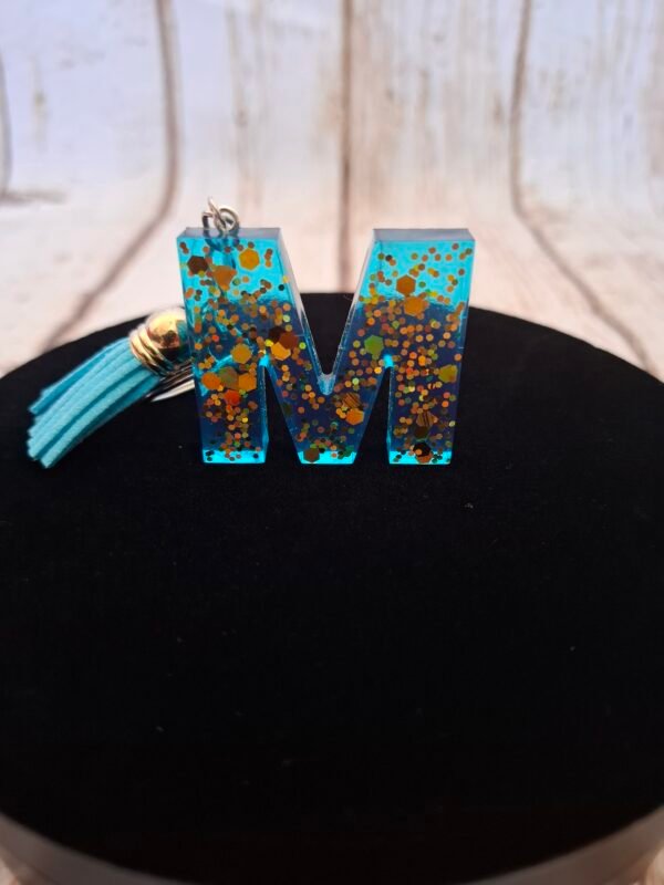 artisanat-cles-trousseau-sac-cadeaux-saint-valentin-003 Bijou de sac lettre M Mystéa, résine brillante décorée de paillettes dorées, avec breloque et pompon rose et vert, un accessoire mixte à offrir ou à garder en souvenir.