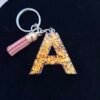 Lettre A en résine, finitions soignées et paillettes dorées, pratique comme porte-clés élégant et original.