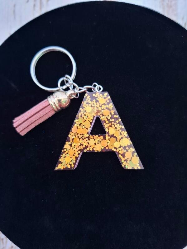Lettre A en résine, finitions soignées et paillettes dorées, pratique comme porte-clés élégant et original.
