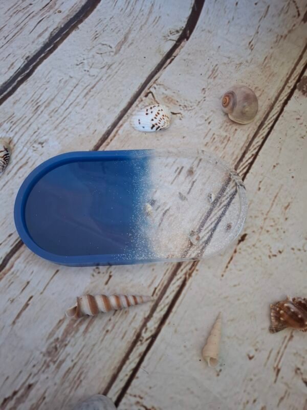 auqatique-outremer-ovale-couleur-personnalisation-creation-008 Vide-poche ovale en résine bleue et transparente, parsemé de mini-coquillages et de paillettes argentées – Élément décoratif unique, parfait pour ajouter une touche marine et élégante à un bureau, une étagère ou un coin de chambre.