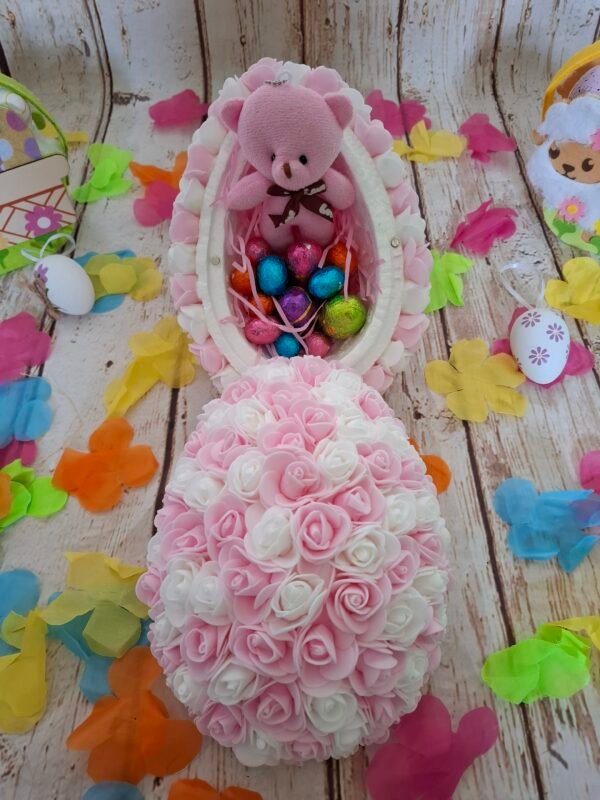 Création florale tendre : œuf rose clair enveloppé de fleurs miniatures, ruban soyeux rose et fermeture sécurisée par de petits aimants, avec une suspension bois lapin charmante.