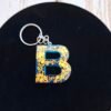 creation-artisanat-turquoise-cles-prenom-epoxy-003 Porte-clés lettre B bleu profond, finition brillante avec touches dorées scintillantes et petit pompon assorti.