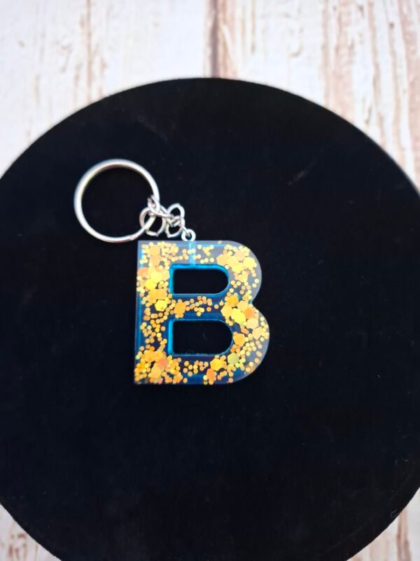 creation-artisanat-turquoise-cles-prenom-epoxy-003 Porte-clés lettre B bleu profond, finition brillante avec touches dorées scintillantes et petit pompon assorti.
