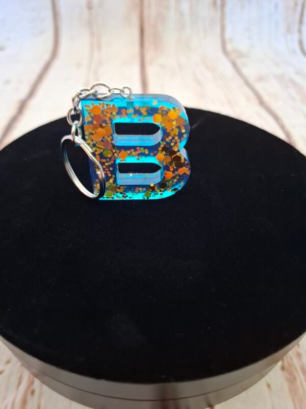 creatrice-floral-solide-couleur-cles-choix-timaiika-005 Lettre décorative B en résine bleutée, reflets dorés intégrés, parfaite comme bijou de sac ou trousseau personnalisé.