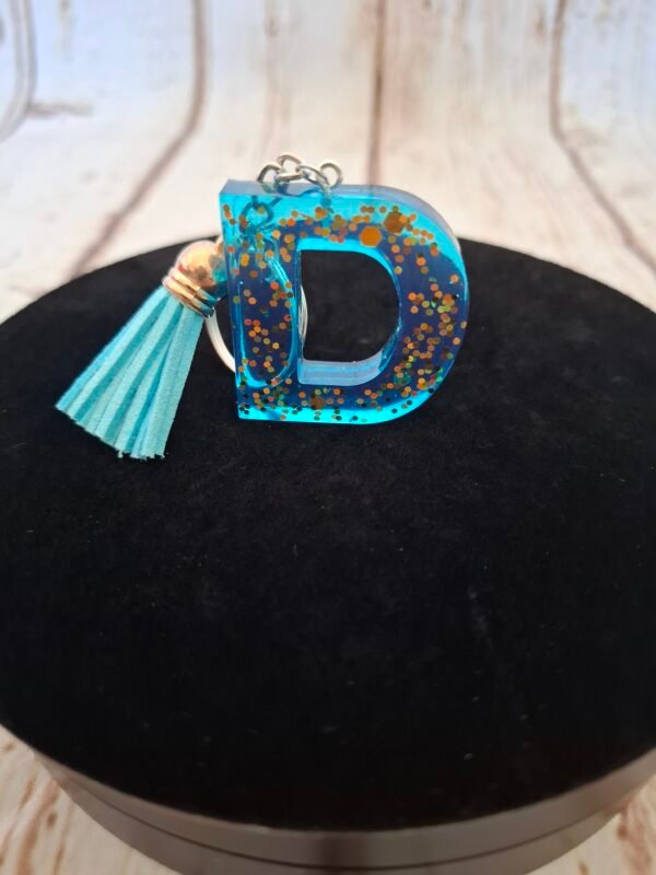 d-resine-bleu-prenom-paillettes-cadeaux-001 Lettre D en resine bleue aux reflets scintillants, realisee artisanalement, accompagnee d un pompon assorti pour embellir un trousseau ou un sac
