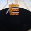 E en Erythéa, lettre stylisée en résine avec détails minutieux et paillettes scintillantes, idéale pour personnaliser un trousseau de clés ou un sac, création artisanale unique et raffinée.