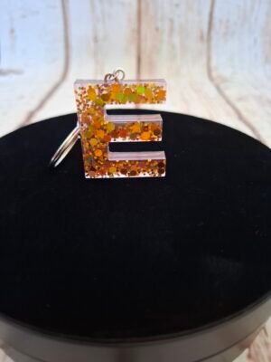 E en Erythéa, lettre stylisée en résine avec détails minutieux et paillettes scintillantes, idéale pour personnaliser un trousseau de clés ou un sac, création artisanale unique et raffinée.