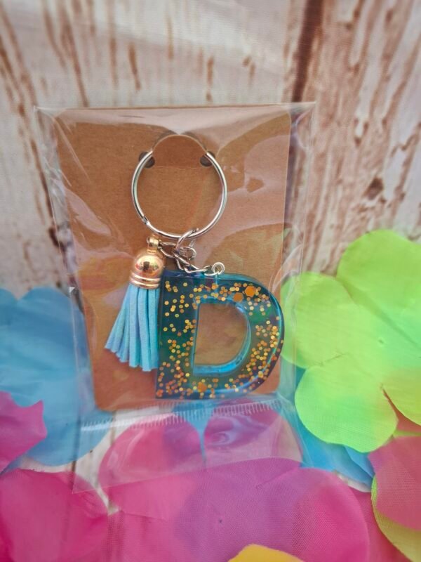 emballage-cadeau-expedition-timaiika-bapteme-decoration-cles-006 D stylisé en matière epoxy nuance marine avec effets lumineux changeants et pompon coordonné pour accessoiriser un sac ou une fermeture éclair