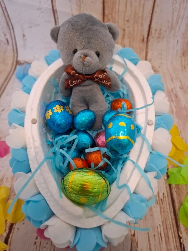 Création festive en polystyrène, ornée de roses tendres et de petites friandises, avec un ourson miniature suspendu.