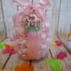Œuf de Pâques Sucré Rose en polystyrène, décoré de mini-roses blanches et roses, orné d’un ruban rose et de petits aimants, avec une délicate suspension en bois gravée d’un lapin.