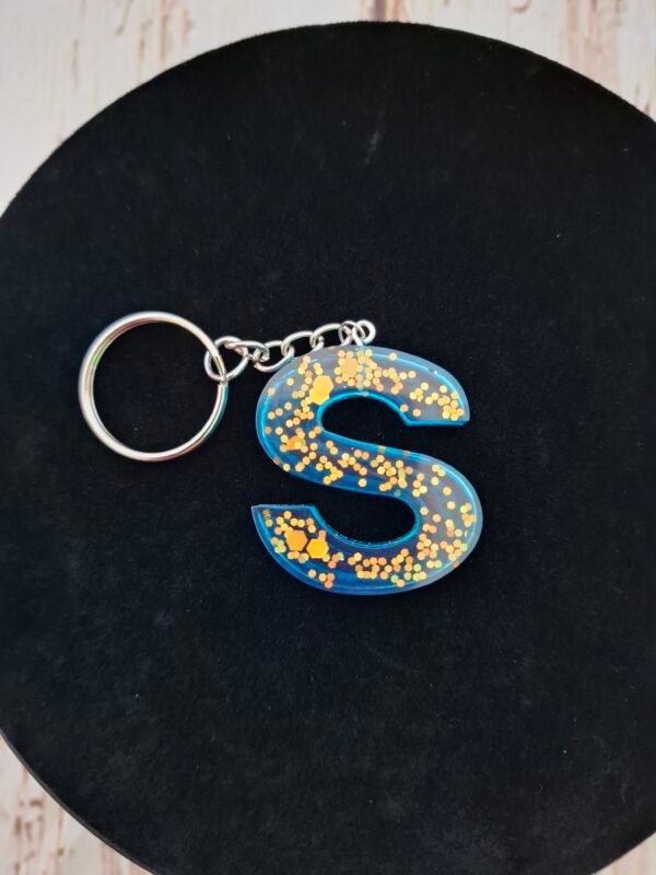 offrir-hommes-anneaux-couleur-bleu-pompon-creations-002 Initiale en résine bleue, finition scintillante avec mousqueton, parfaite pour cadeau de Noël ou anniversaire.