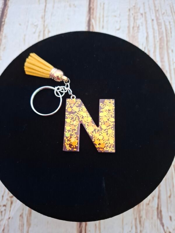 Initiale délicate en matière brillante, ornée de touches roses et dorées, petite création à apprécier au quotidien.