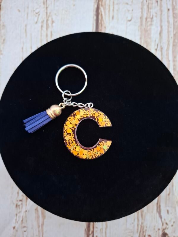 Porte-clés C en résine rose Célunéa, délicatement parsemé de reflets scintillants qui captent la lumière.