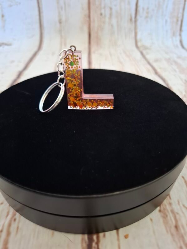 resine-epoxy-l-porte-clefs-creations-prenoms-initiales-offrir-hommes-001 Lettre L délicatement façonnée à la main dans une résine rosée scintillante, montée sur un porte-clés avec un pompon élégant pour accessoiriser sacs et trousseaux.