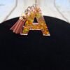 Lettre A en résine faite main, avec de délicates paillettes dorées et un petit pompon, parfaite pour personnaliser un trousseau de clés.