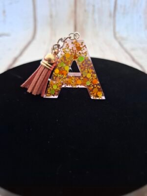 Lettre A en résine faite main, avec de délicates paillettes dorées et un petit pompon, parfaite pour personnaliser un trousseau de clés.
