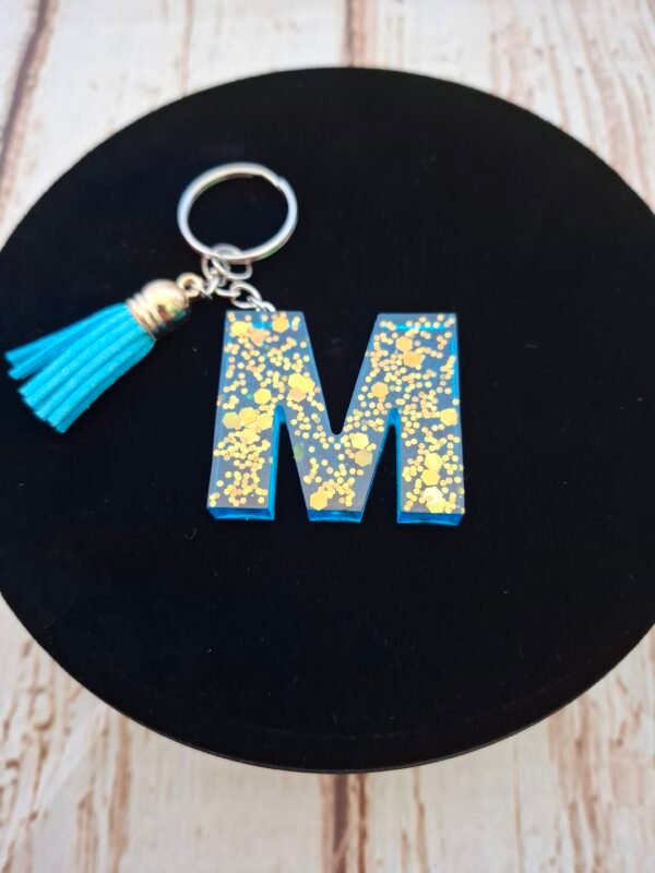 rose-couleurs-anneaux-mousqueton-offrir-hommes-femmes-002 Lettre M en Mystéa en résine bleue étincelante avec paillettes dorées, montée sur porte-clés avec mousqueton et pompon, idéale comme cadeau ou souvenir pour Noël ou la Saint-Valentin.