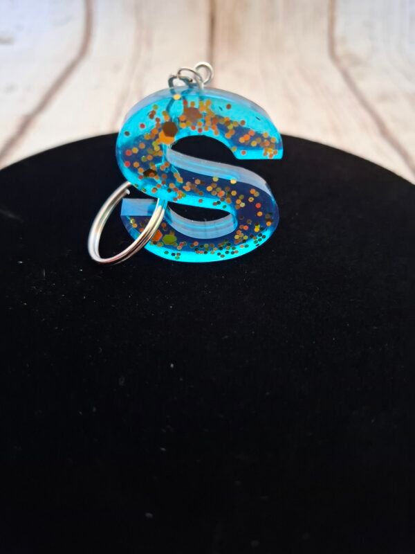 s-resine-epoxy-cadeaux-rose-paillettes-dorees-prenom-001 S en Sorynelle lettre en résine rose avec paillettes dorées, montée sur un porte-clés élégant pour offrir à un homme ou une femme.