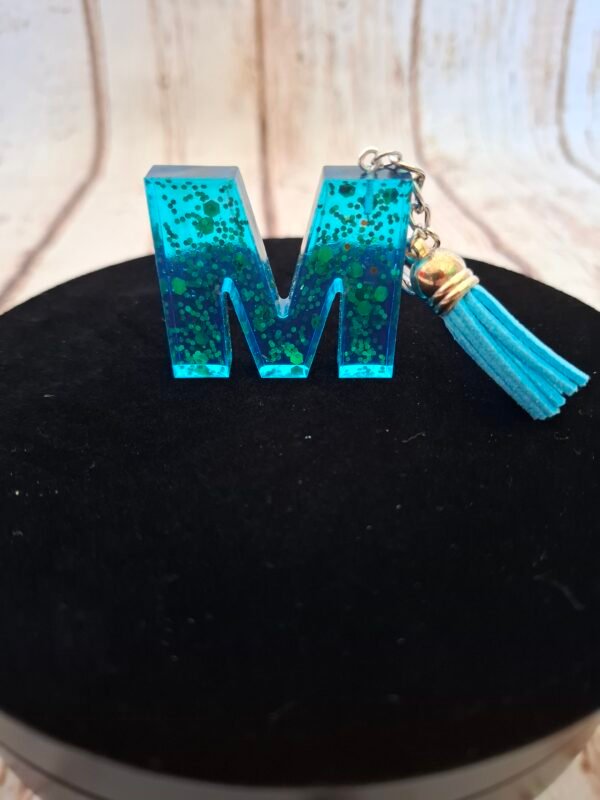 transparent-lumineux-scintillant-brillant-beau-qualité-joli-005 Création artisanale initiale M en Mystéa, résine colorée avec touches dorées scintillantes, accompagnée d’un pompon fantaisie, pratique pour clés, sacs ou trousseaux.