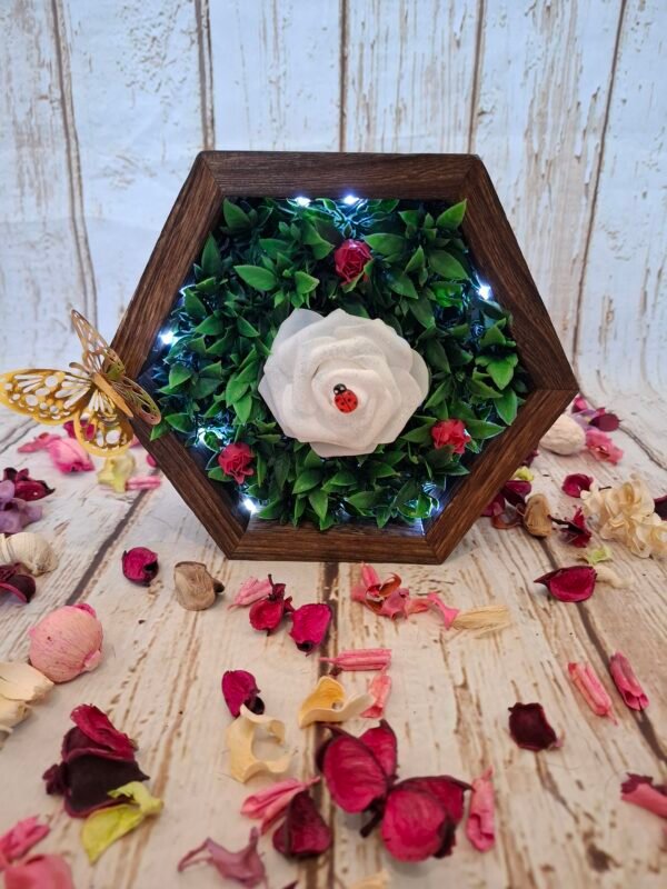 Une rose blanche en mousse trône au milieu, subtilement décorée de paillettes scintillantes qui captent la lumière.