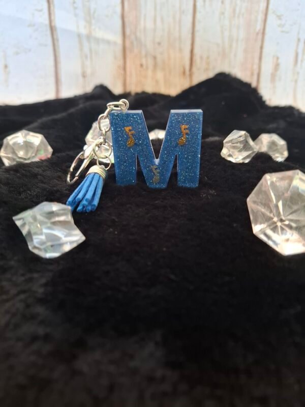 portecles-resine-musique-cadeaux-epoxy-paillettes-notes-sacs-001 Lettre M en résine artisanale, décorée de fines paillettes dorées et montée sur un porte-clés avec mousqueton, parfaite pour un cadeau original.