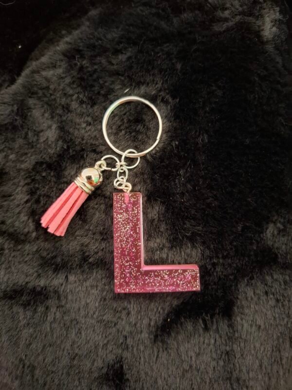 resine-portecles-rose-paillettes-argentees-sacs-cadeaux-anneaux-mousqueton-001 Lettre L en Lollyglow montée sur un porte-clés avec un pompon charmant, parfaite pour personnaliser clés ou sacs à main.